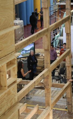 A view through a section of a wooden structure where students and faculty are visible talking.