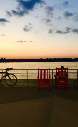 A bicycle and three red chars line a railing in front of the Tennessee River at sunset