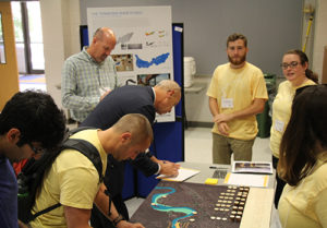 A group of people gathered around a table with a model of the watershed.