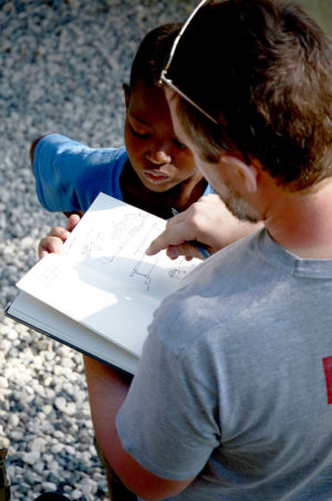 A male University of Tennessee student shows his design sketchbook to a young Haitian boy.
