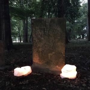 A headstone at night, illuminated by two paper bag lanterns.