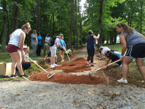 A group of students with rakes work on spreading dirt on a path.