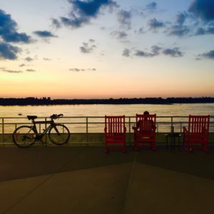 A bicycle and three red chars line a railing in front of the Tennessee River at sunset
