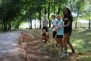 A group of five University of Tennessee students with rakes work alongside the path through the cemetery.