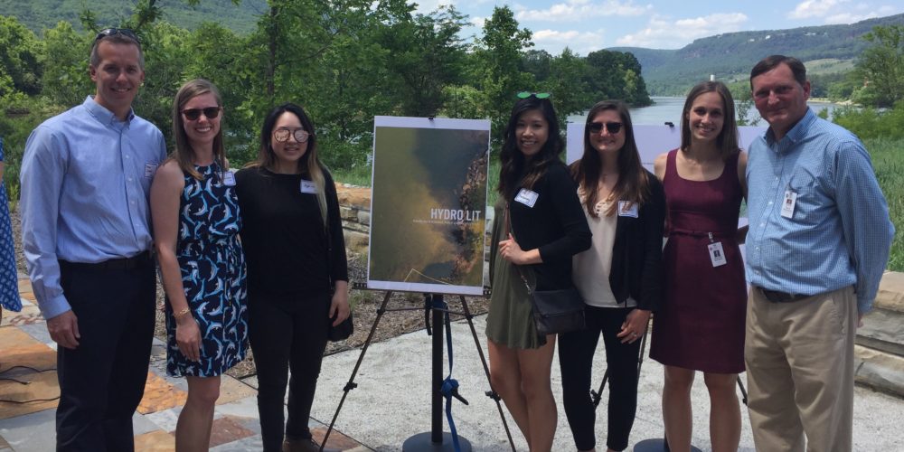 Students and faculty members stand next to a poster-sized version of the book's cover on an easel.