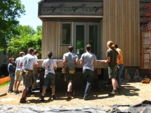 A group of people works on assembling part of the exterior of the house.