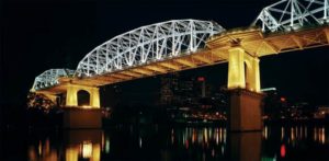 A bridge over the Tennessee River at night, lit with yellow lights on the underside and white light along the top.