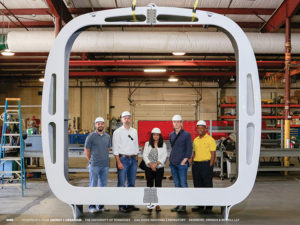 A group of people in hardhats stand with one of the structural elements of AMIE.