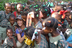 A large group of Haitian children in school uniforms surround a female University of Tennessee student.