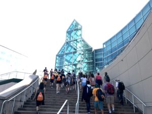 A group of high school students climb stairs towards a building that resembles a glass castle.