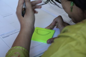 A student sketches an idea on a bright green post-it note.