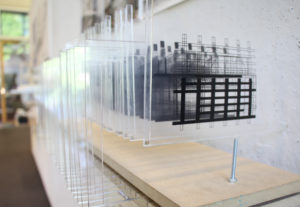 A detail shot of a series of plexiglass "boards" with black and white sketches on them standing vertically along a wall.