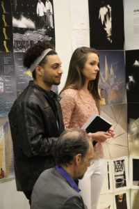 Two students stand and listen during a critique