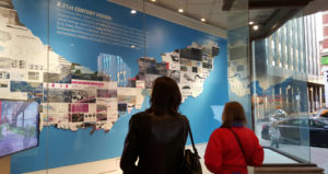 Two women look at an exhibit on the wall.