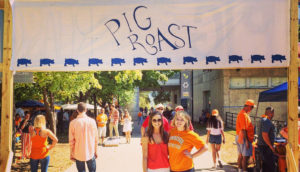 Two girls stand together under a Pig Roast banner.