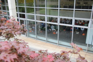 A group of families attending an open house seen from the exterior of the Art + Architecture Building looking through the windows.