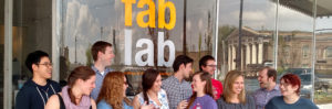 A group of students stands on the sidewalk in front of the Fab Lab.