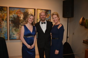 A man and two women in an art gallery in black tie and evening wear