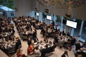 An overview of a large banquet room with round tables full of people.