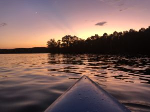 tip of a kayak over the water with orange sky