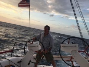 Buzz Goss stands at the helm of a sailboat