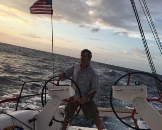Buzz Goss stands at the helm of a sailboat