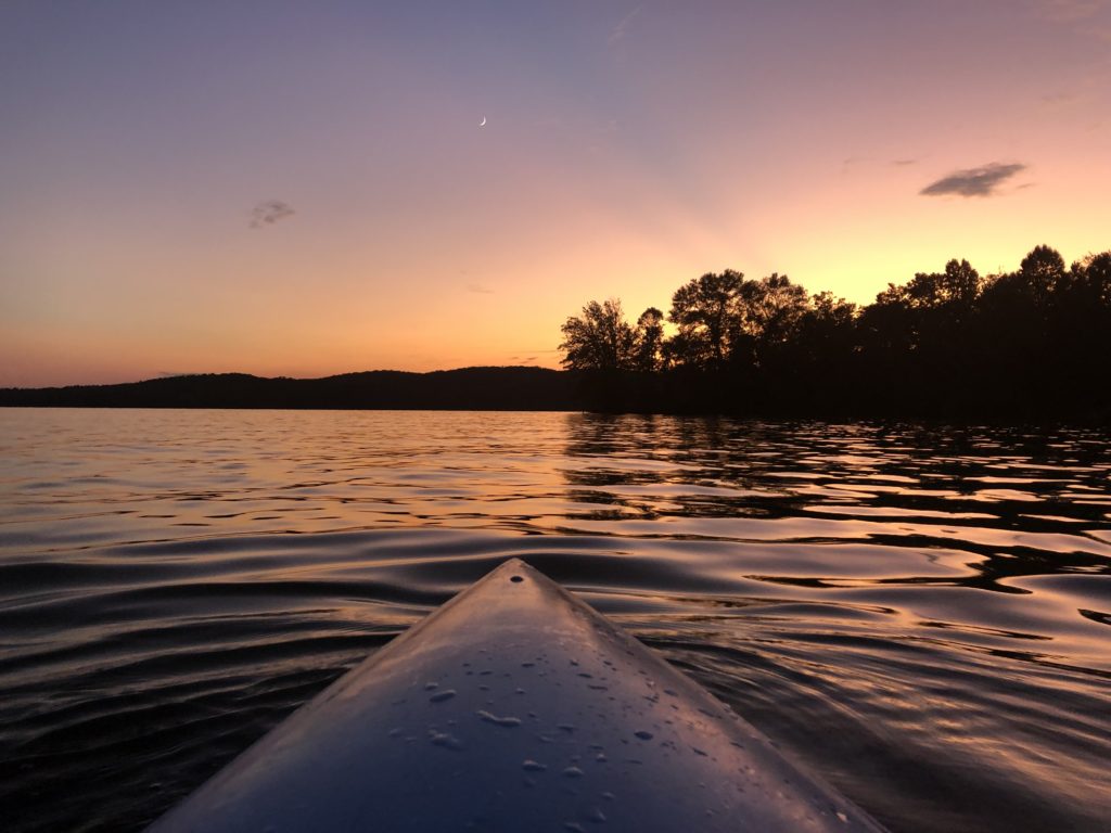 Nose of a kayak with river and sunset in background