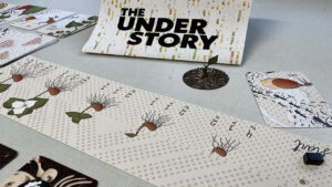 Elements of The UNDERstory card game spread across a table.
