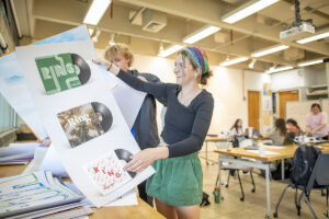 Student shuffles through large-format prints of designs.