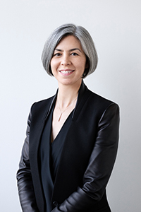 A color headshot of Kim Yao with a short, silver bob. She is wearing a necklace, a black blouse with a black blazer overtop. She is looking directly at the camera with a smile.