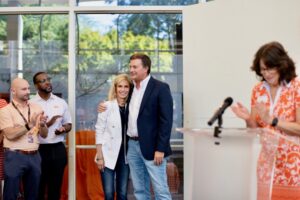 Jeff and Marla Gerber, in focus, hug and smile. They receive applause from Brian Broyles, far left, and Craig Jackson, left, and Pamela Treacy, far right.