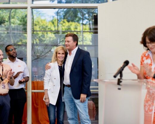 Jeff and Marla Gerber, in focus, hug and smile. They receive applause from Brian Broyles, far left, and Craig Jackson, left, and Pamela Treacy, far right.