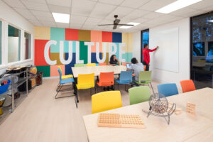 Interior a multipurpose room at Park Center Woodland Renovation. The back wall features a custom mural of blocked colors featuring the word, "culture."