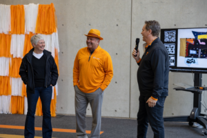 Cindy, left, and George Ewart, center, stand with hands in their pockets during a presentation on the CoAD Exchange led by Dean Jason Young, right.
