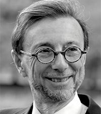 Black-and-white headshot of a man with short hair and round glasses, wearing a suit and tie.